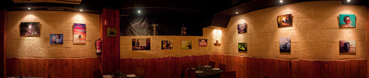 Panorama of a photo exhibition: framed prints lit by spotlights along the curved stone walls of a dark room