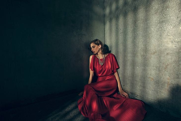 Film noir-style photo of a woman in a red dress seated against a dark stone wall