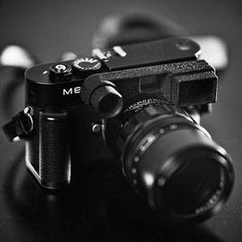 Black-and-white close-up of a mirrorless rangefinder-style camera with attached lens, illustrating an article about mirrorless cameras