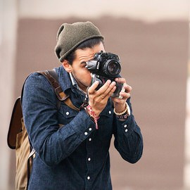 A man in a beanie and denim shirt raising a camera to take a photo outdoors, from a Phlearn Features interview with photographer Grant Legan (Part 3 of 3)
