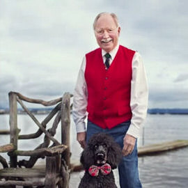 An older man in a red vest standing on a dock with a black poodle wearing a bow tie, overcast sky in the background, demonstrating how to recover detail from a sky in Photoshop