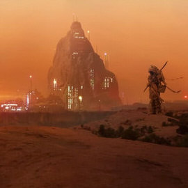 A cloaked figure standing before a fortress-like rock formation glowing with lights at dusk in a desert, behind-the-scenes photo from 'A Dark Force' advanced compositing shoot