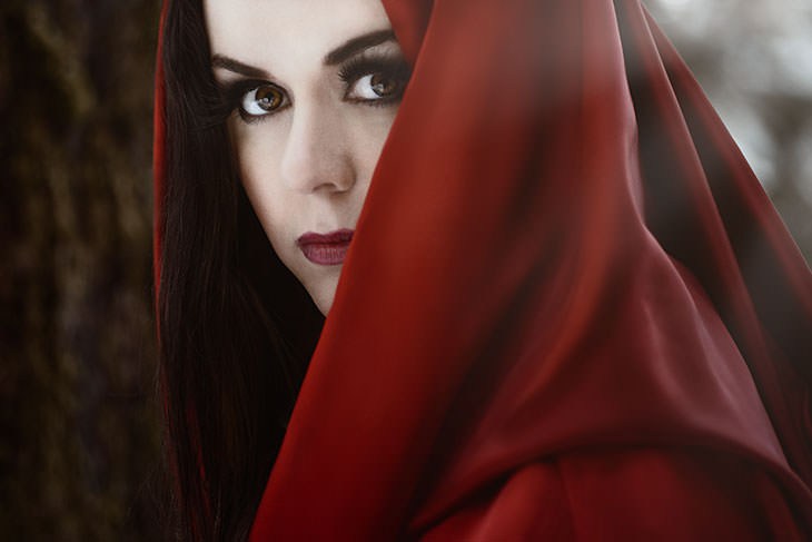 Moody portrait of a woman wrapped in a deep red hooded cloak