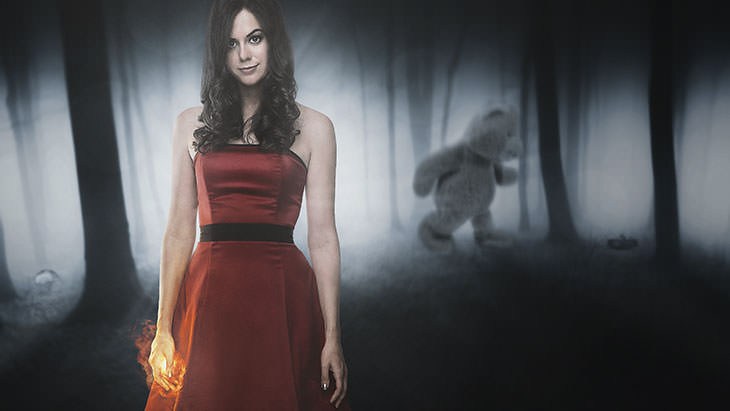 Full-body portrait of a woman in a red dress in a foggy, dimly lit forest with a shadowy figure in the background