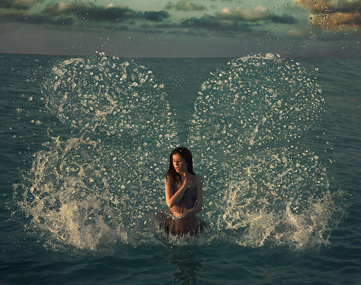 Mandy Rosen self-portrait standing waist-deep in the sea at dusk, splashing water fanned out behind her like wings