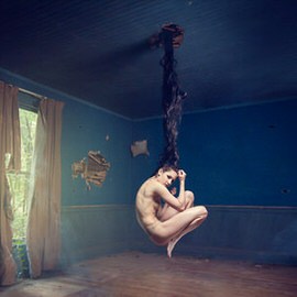 Nude figure curled up and suspended by dark hair from the ceiling of a blue room, illustrating how to suspend a person in the air in Photoshop