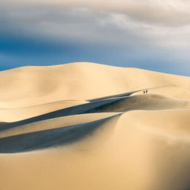 Wide panoramic view of desert sand dunes with tiny figures walking along the ridge, illustrating gear suggestions for shooting panoramic photos