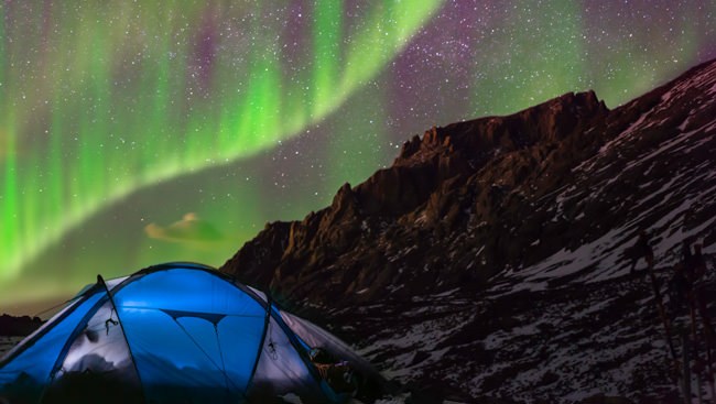 Green aurora borealis over a mountain ridge above a lit blue camping tent at night, Photoshop Northern Lights tutorial thumbnail
