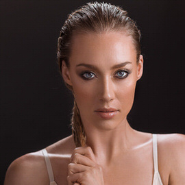 Close-up portrait of a woman with slicked-back hair and smooth retouched skin holding her braid against a dark background, thumbnail for the Retouching 201 course