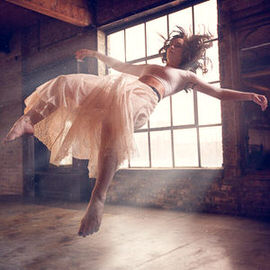 Woman in a flowing white dress levitating in mid-air inside a sunlit industrial room, example for the beginners guide to levitation photography