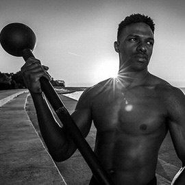 Black and white photo of a shirtless man holding a large studio light against a bright sunburst sky, example for processing black and white photos in Lightroom