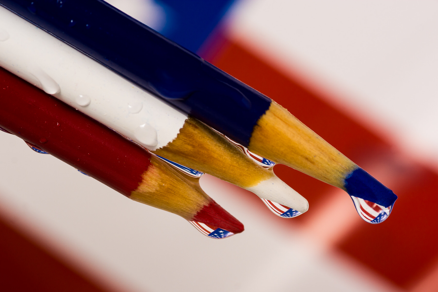 Macro of red, white and blue colored pencils, each tip holding a water drop that reflects an American flag