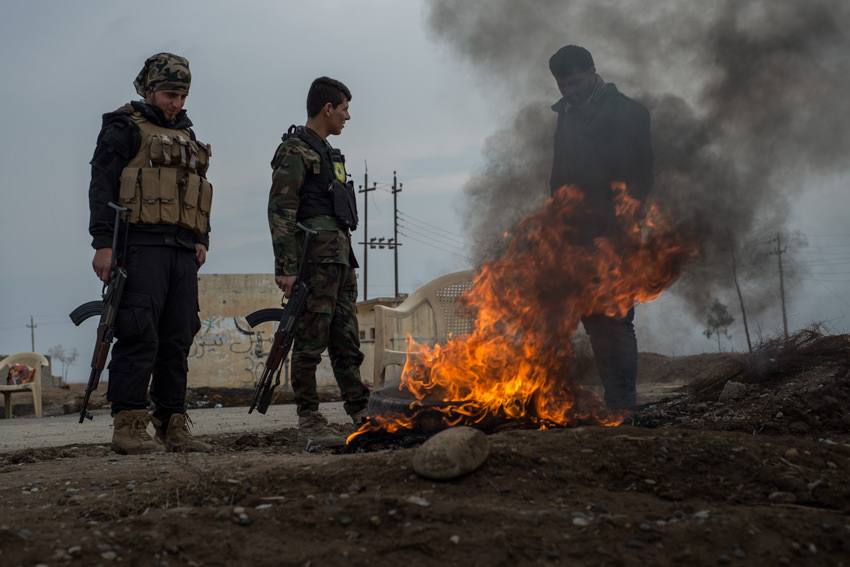 Conflict photographer Felipe Passolas’s photo of two armed fighters in combat gear by a burning fire on a dirt road as a man watches through the smoke