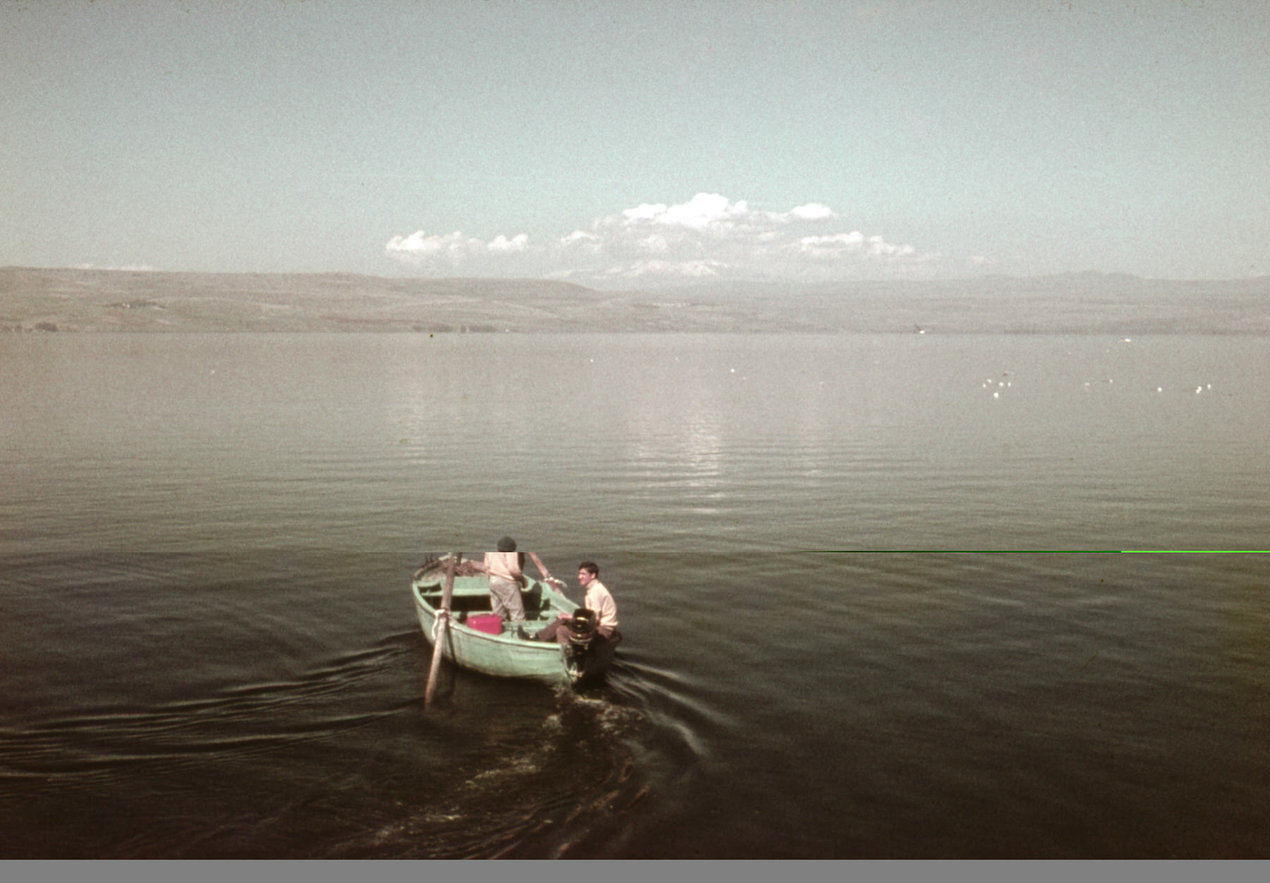 Old color slide of two men in a small green rowboat heading out across a calm lake under a hazy sky