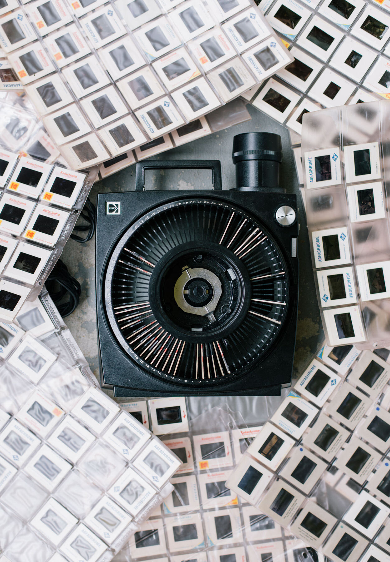 Black carousel slide projector seen from above, surrounded by plastic sleeves full of mounted slides