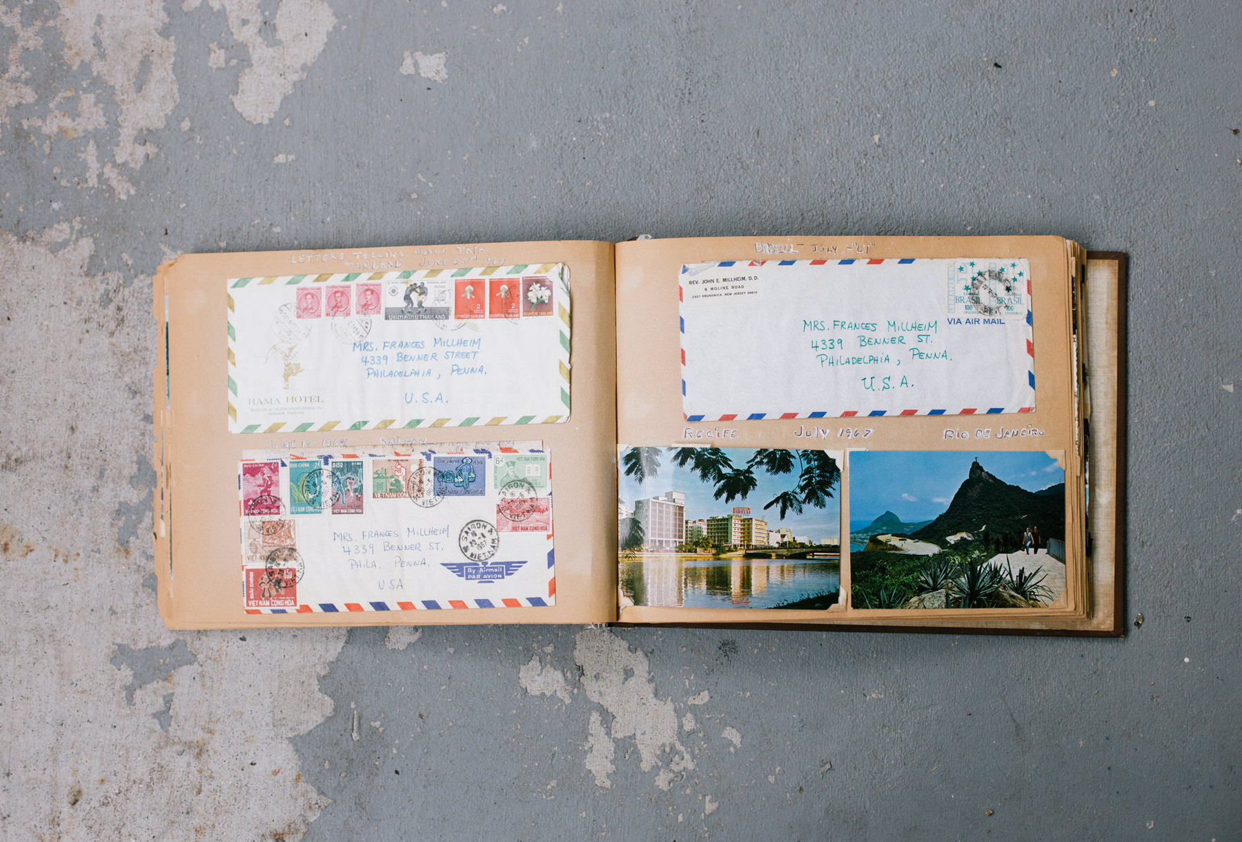 Open scrapbook with stamped airmail envelopes addressed to Philadelphia and two color postcards pasted on its pages