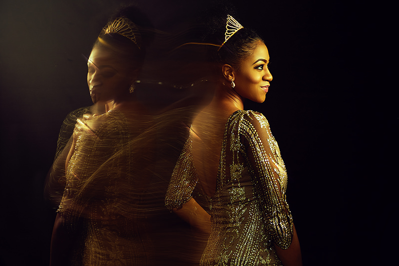 Woman in a tiara and gold dress smiling over her shoulder, a ghosted motion-blurred copy of her behind