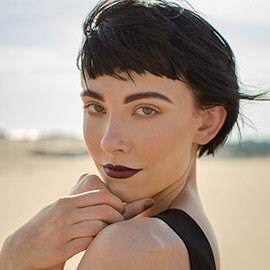 Close-up portrait of a woman with short dark hair and dark lipstick against a desert background, thumbnail for the Lightroom Classic 101 and 201 courses