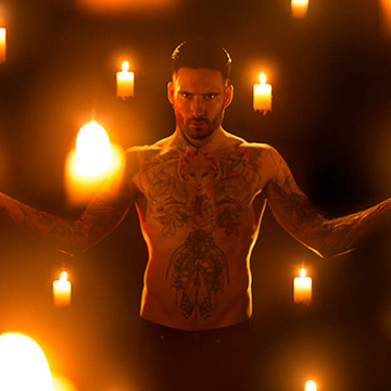 Shirtless tattooed man with arms outstretched composited among glowing candles in a dark scene, example for essential Photoshop compositing tools and techniques