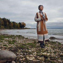 Person in a patterned coat standing on a rocky beach holding a camera, example for importing, organizing and adding metadata to photos in Lightroom Classic