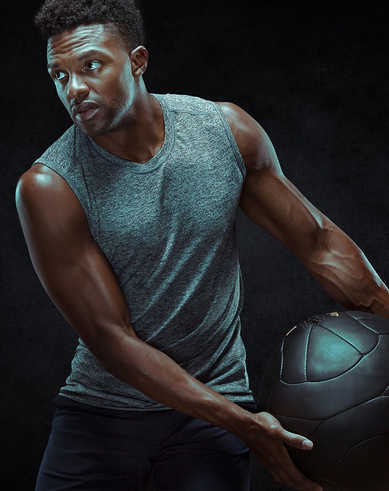 Athlete holding a medicine ball at his side, low-key studio lighting