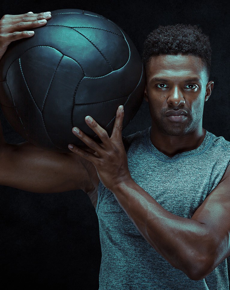 Athlete with a medicine ball on his shoulder against a black background