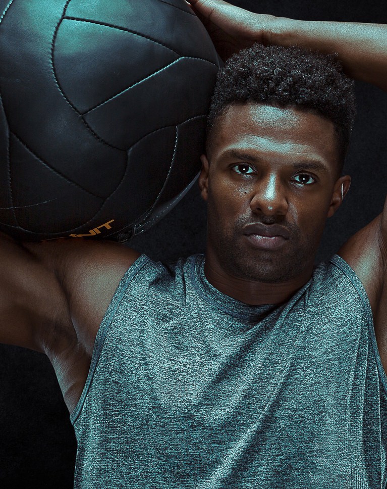 Athlete holding a medicine ball on his shoulder, dark studio portrait
