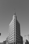 Black and white photo of a tall, narrow triangular skyscraper against a clear sky