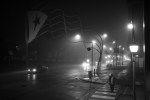 Black and white night photo of a rain-soaked city street lit by streetlights