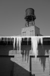 Black and white photo of icicles hanging from a rooftop beneath a water tower