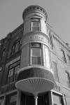Black and white photo of an ornate corner building with a rounded turret and bay windows