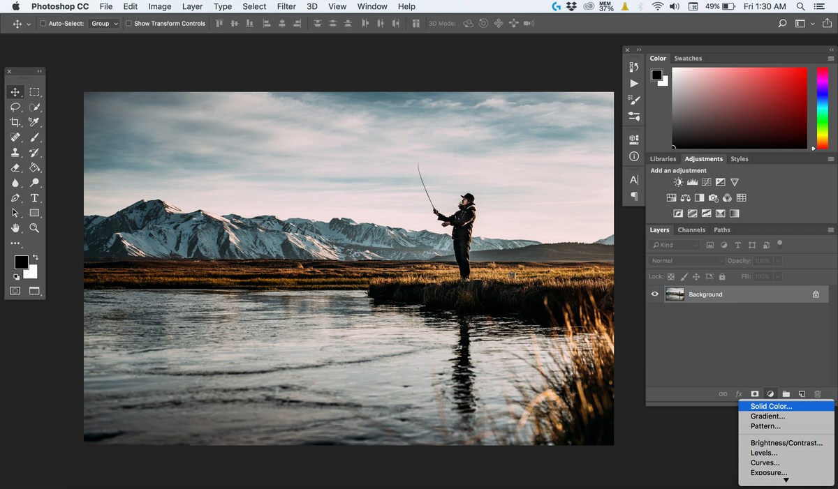 Selecting Solid Color from the adjustment layer menu above a landscape photo of a person fly fishing