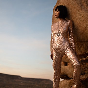Woman in a metallic geometric-patterned bodysuit leaning against a large rock at golden hour, example for dodging and burning in Lightroom using range masking