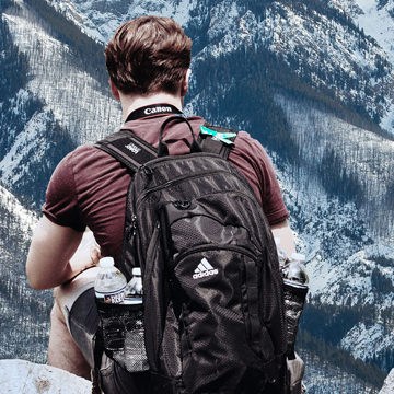 Hiker seen from behind wearing a backpack with water bottles overlooking snowy mountain peaks, example for matching colors for compositing in Photoshop