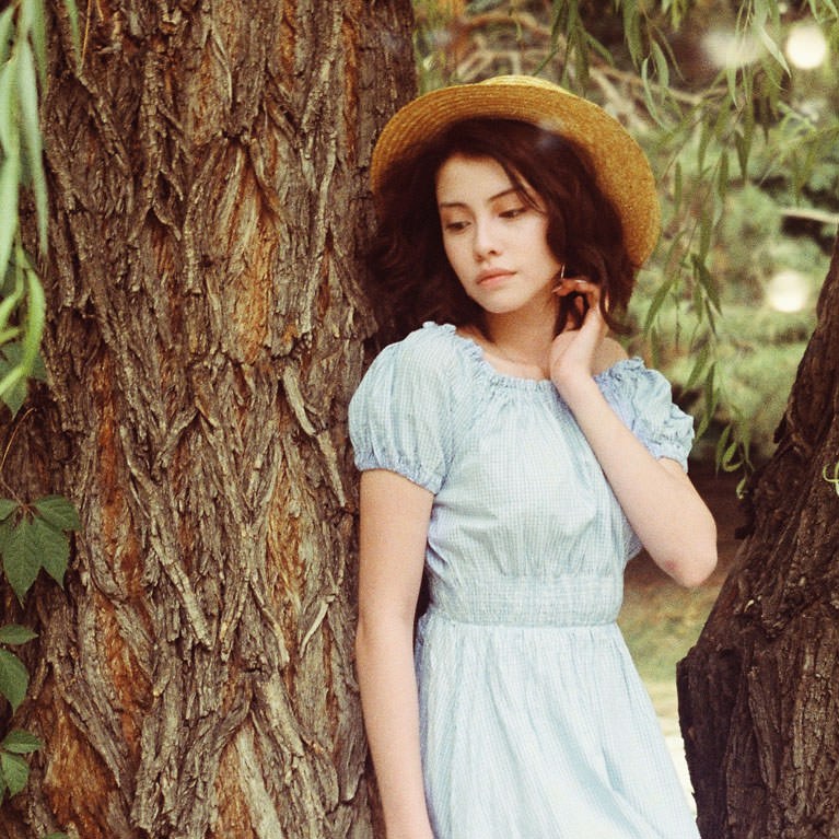Woman in a light blue puff-sleeve dress leaning against a textured tree trunk, example for color toning in Photoshop