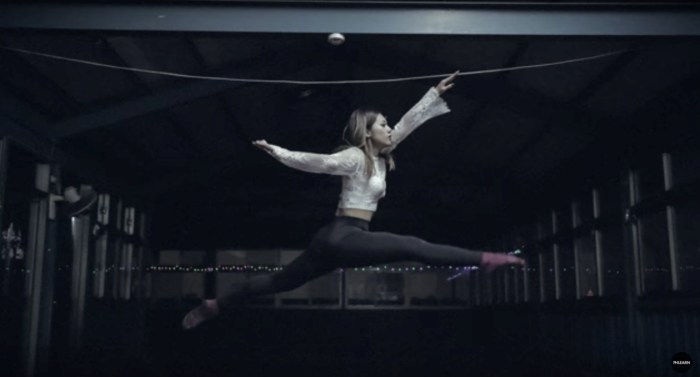 Dancer in a split leap in a dark hall, with slight blur in her hands and feet