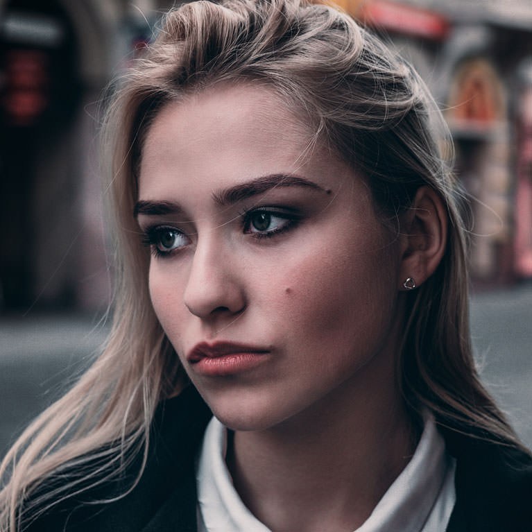 Close-up portrait of a blonde woman with striking eyes looking off to the side on a city street, example for skin retouching basics in Photoshop