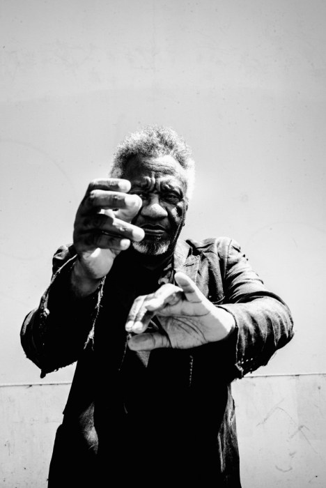 Black-and-white portrait of Donald Byrd reaching both hands toward the camera, fingers spread