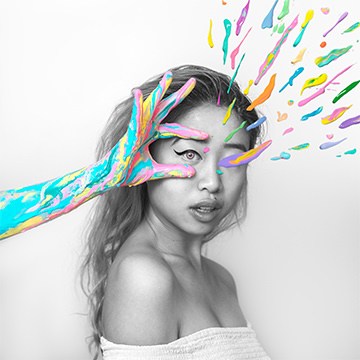 Black and white portrait of a woman with a colorful painted hand splashing paint across her face, example for creating a paint splash effect in Photoshop with Natalia Seth