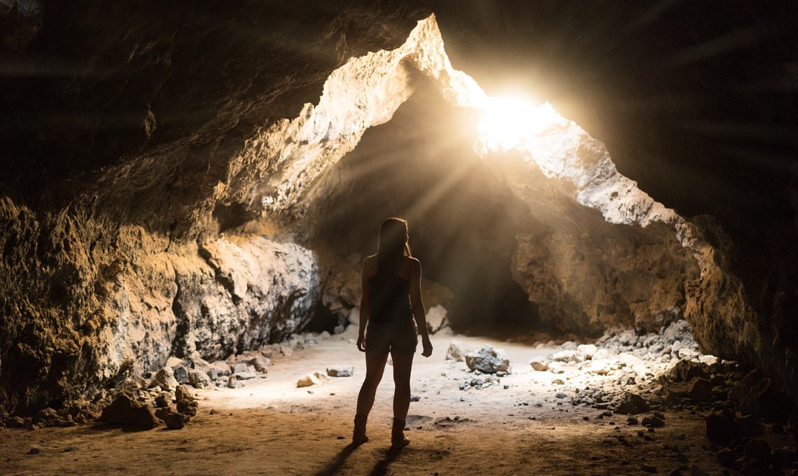 Silhouette of a person standing in a rocky cave opening with sunlight streaming through, after the Light Rays action is applied