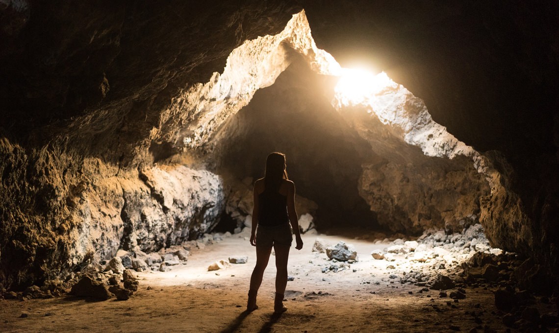 Silhouette of a person standing in a rocky cave opening with sunlight streaming through, before the Light Rays action is applied