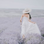 Woman in a white dress and sun hat walking through a lavender field, edited with the Neutral Airy presets