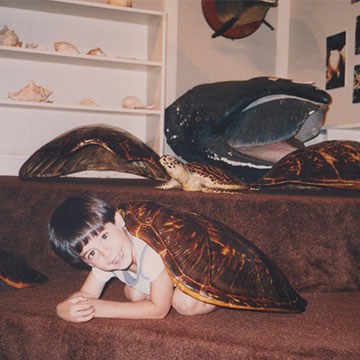 Vintage childhood photo of a young boy lying on a couch surrounded by large decorative turtle shells