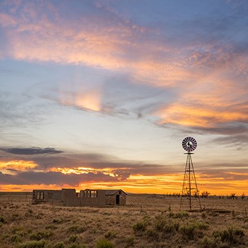 Sunset sky over an abandoned farmhouse and windmill on the prairie, with warm HDR-processed clouds