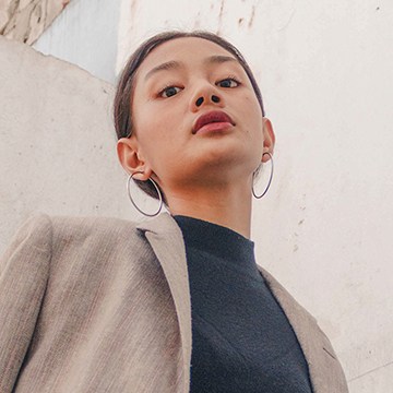 Portrait of a woman with hoop earrings photographed against a plain white wall, demonstrating how to turn your favorite looks into Lightroom presets