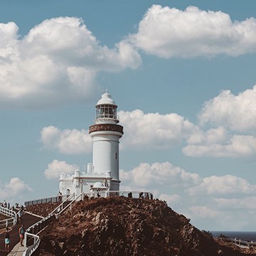 A white lighthouse on a rocky cliff under a bright blue sky with clouds, demonstrating the Sky Replacement tool in Photoshop and how to pick the right sky