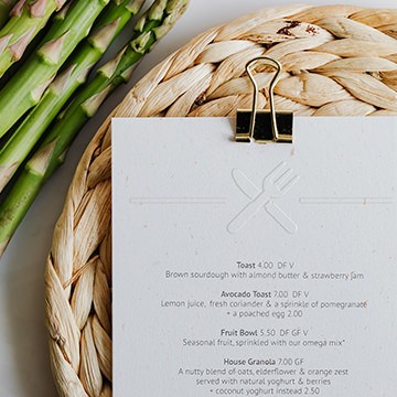 Asparagus spears beside a woven placemat and a card embossed with a fork and knife icon, demonstrating how to add a realistic embossed effect to text and logos in Photoshop