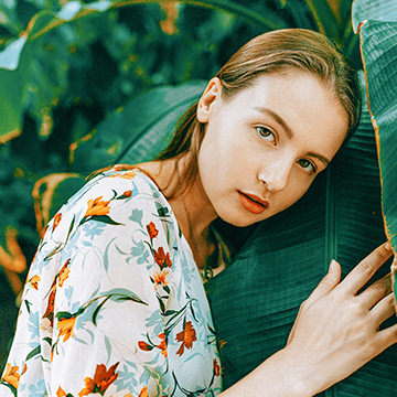 Woman in a floral top leaning against large green leaves, illustrating the difference between saturation and vibrance in Photoshop
