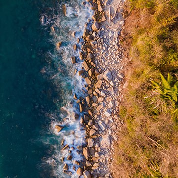 Aerial drone photo of waves crashing on a rocky coastline next to green land, illustrating how to take better drone photos