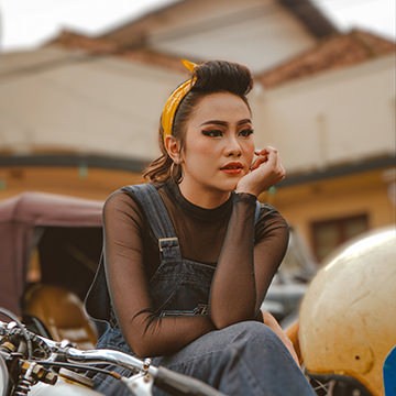 Woman in overalls leaning on a motorbike with the background softly blurred, demonstrating how to automatically blur backgrounds in Photoshop